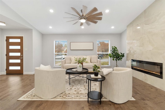 living room featuring a tiled fireplace, ceiling fan, and wood-type flooring