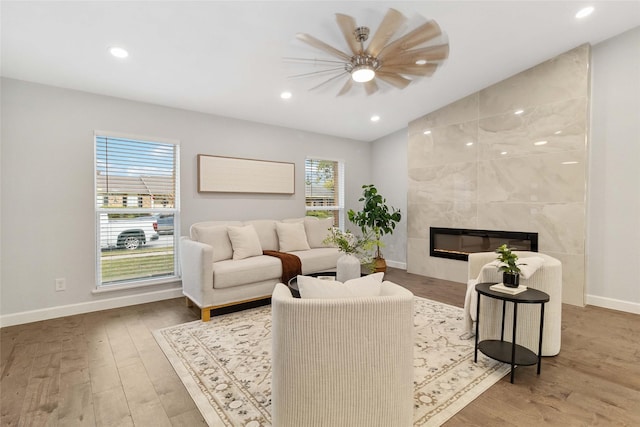 living room featuring a tiled fireplace, ceiling fan, and wood-type flooring