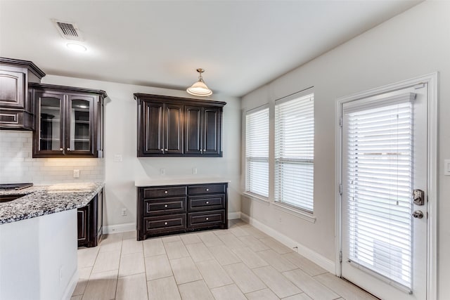 kitchen with dark brown cabinetry, backsplash, and light stone countertops