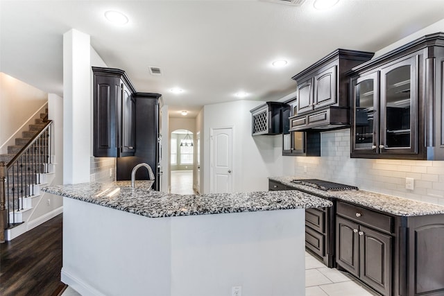 kitchen with decorative backsplash, stainless steel gas cooktop, kitchen peninsula, light stone countertops, and dark brown cabinets