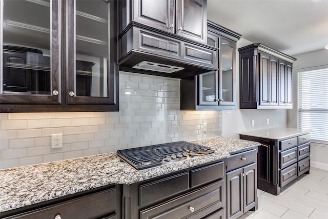 kitchen with stainless steel gas stovetop, custom exhaust hood, dark brown cabinetry, and decorative backsplash