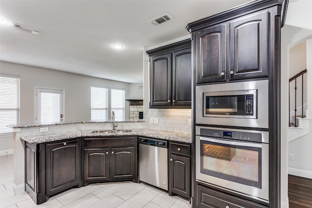 kitchen featuring sink, stainless steel appliances, kitchen peninsula, and light stone countertops