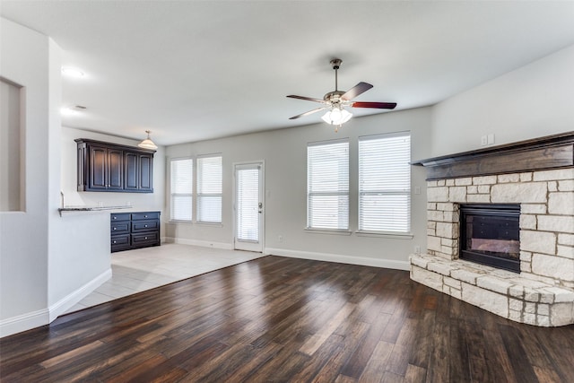 unfurnished living room with a stone fireplace, hardwood / wood-style floors, and ceiling fan