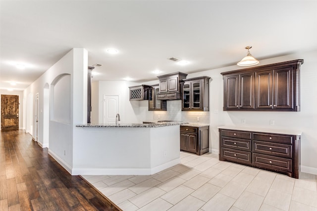 kitchen featuring sink, backsplash, light stone counters, dark brown cabinets, and light wood-type flooring