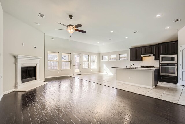 kitchen with light tile patterned floors, lofted ceiling, stainless steel appliances, and a center island with sink