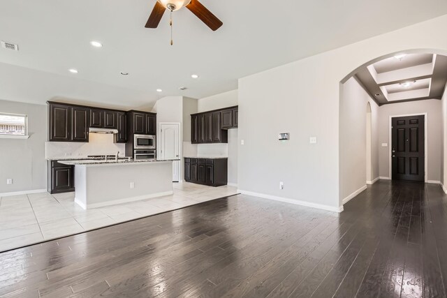 kitchen with ceiling fan, light stone countertops, an island with sink, lofted ceiling, and appliances with stainless steel finishes