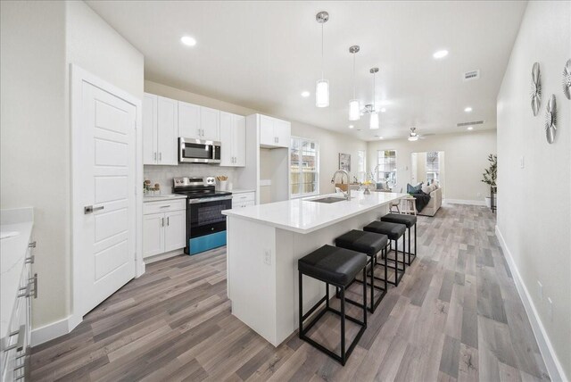 kitchen featuring white cabinetry, stainless steel appliances, a kitchen breakfast bar, pendant lighting, and a kitchen island with sink