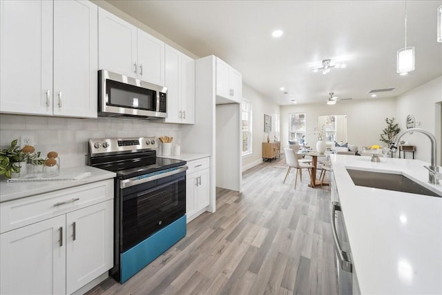 kitchen featuring appliances with stainless steel finishes, light wood-type flooring, sink, pendant lighting, and white cabinets