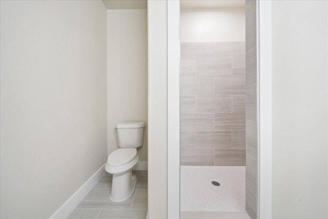 bathroom featuring tile patterned flooring, toilet, and tiled shower