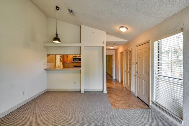 unfurnished living room with a textured ceiling, light carpet, and vaulted ceiling