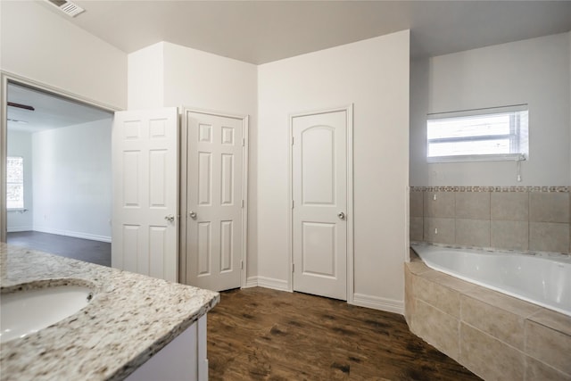 bathroom featuring tiled bath, vanity, hardwood / wood-style flooring, and a healthy amount of sunlight