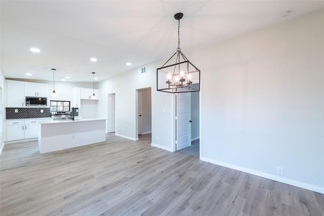 kitchen with white cabinets, stainless steel microwave, hanging light fixtures, and a kitchen island with sink