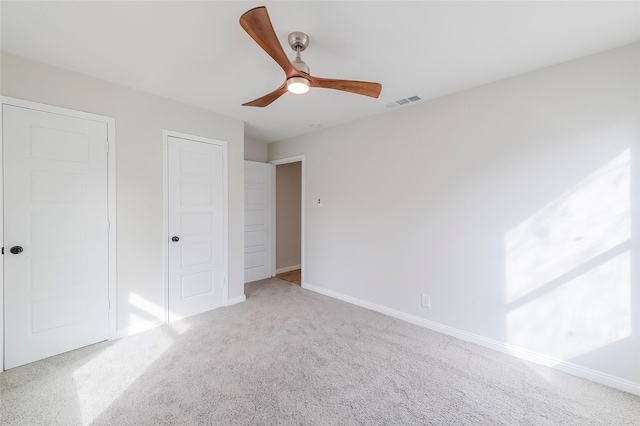 unfurnished bedroom featuring multiple closets, light carpet, and ceiling fan