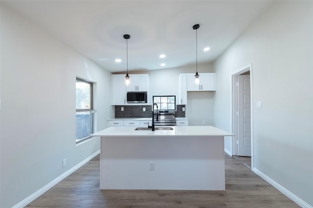 kitchen featuring stainless steel microwave, sink, hanging light fixtures, an island with sink, and white cabinets