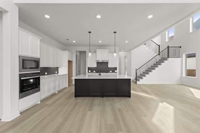 kitchen featuring black microwave, stainless steel oven, decorative light fixtures, a kitchen island with sink, and white cabinets