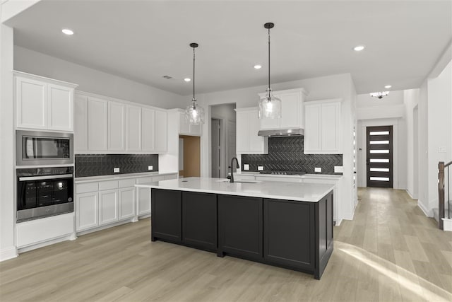 kitchen with built in microwave, pendant lighting, oven, a center island with sink, and white cabinetry