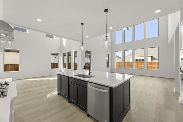 kitchen featuring a kitchen island with sink, sink, light hardwood / wood-style flooring, dishwasher, and hanging light fixtures