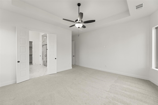 unfurnished bedroom with a tray ceiling, ensuite bath, ceiling fan, and light colored carpet