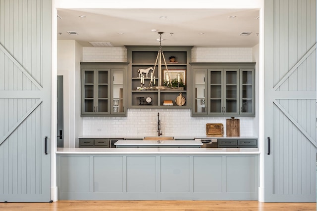 bar with backsplash, gray cabinets, hanging light fixtures, and sink