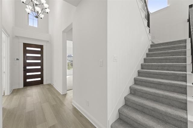 foyer entrance with light hardwood / wood-style flooring, a towering ceiling, and a notable chandelier