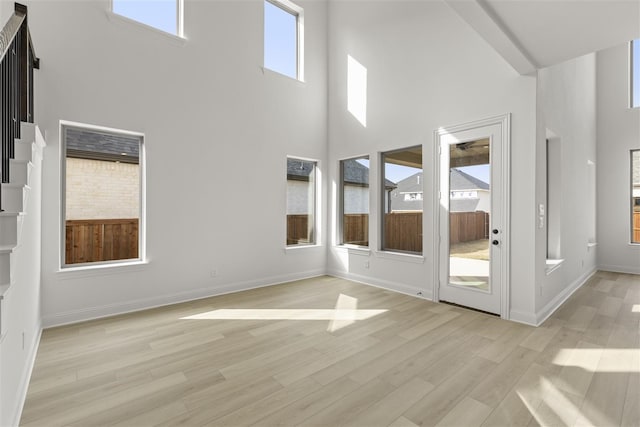 unfurnished living room with light wood-type flooring and a high ceiling