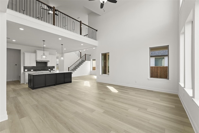 living room featuring ceiling fan, light hardwood / wood-style flooring, and a towering ceiling