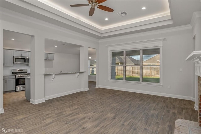 unfurnished living room with a fireplace, dark hardwood / wood-style floors, a raised ceiling, and plenty of natural light