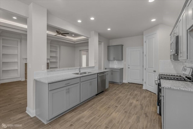 kitchen featuring appliances with stainless steel finishes, light stone counters, ceiling fan, sink, and light hardwood / wood-style flooring