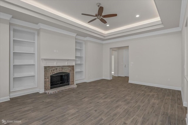 unfurnished living room featuring ceiling fan, dark hardwood / wood-style floors, a raised ceiling, and a brick fireplace