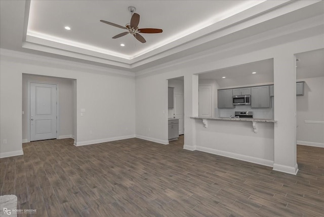 unfurnished living room with a raised ceiling, ceiling fan, and dark hardwood / wood-style flooring