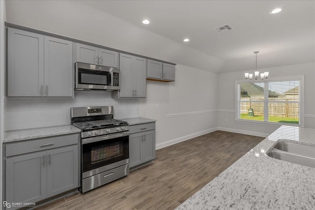 kitchen with gray cabinetry, light stone counters, hardwood / wood-style floors, decorative light fixtures, and appliances with stainless steel finishes