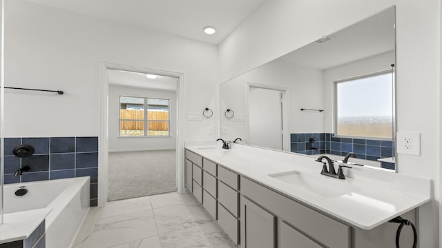 bathroom with double vanity, marble finish floor, a tub to relax in, and a sink