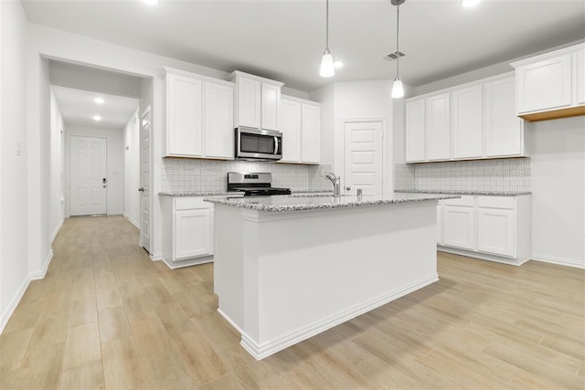 kitchen with white cabinets, a center island with sink, light stone countertops, light wood-type flooring, and appliances with stainless steel finishes