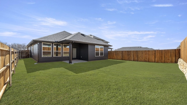 back of property with a fenced backyard, a yard, and roof with shingles