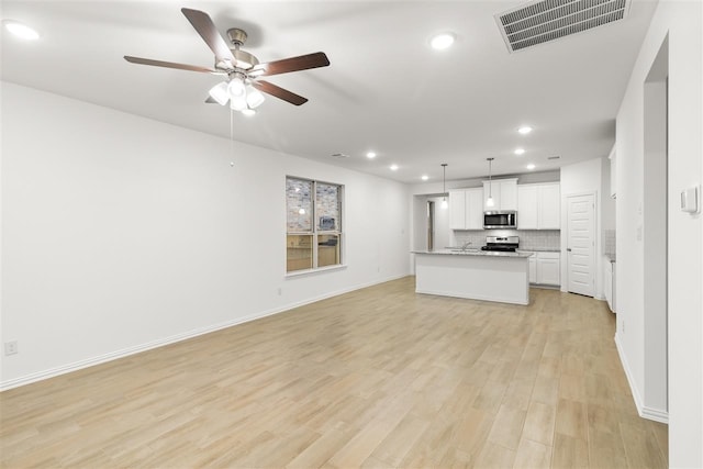 kitchen with white cabinetry, stainless steel appliances, pendant lighting, light hardwood / wood-style floors, and a center island with sink