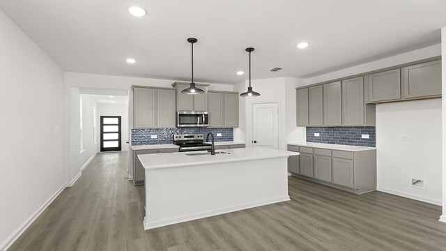 kitchen featuring stainless steel appliances, an island with sink, pendant lighting, light hardwood / wood-style floors, and white cabinets