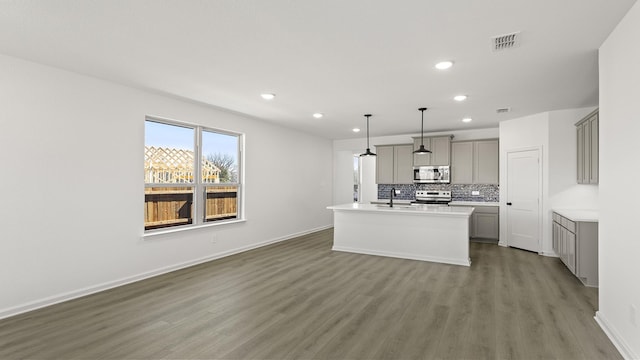 kitchen with light countertops, appliances with stainless steel finishes, hanging light fixtures, gray cabinets, and a center island with sink