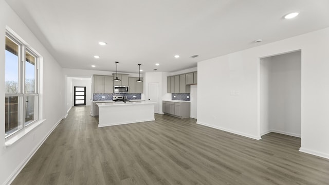 kitchen featuring gray cabinetry, stainless steel microwave, light countertops, hanging light fixtures, and an island with sink