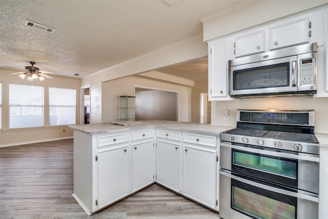 kitchen with kitchen peninsula, light hardwood / wood-style flooring, a textured ceiling, appliances with stainless steel finishes, and white cabinetry