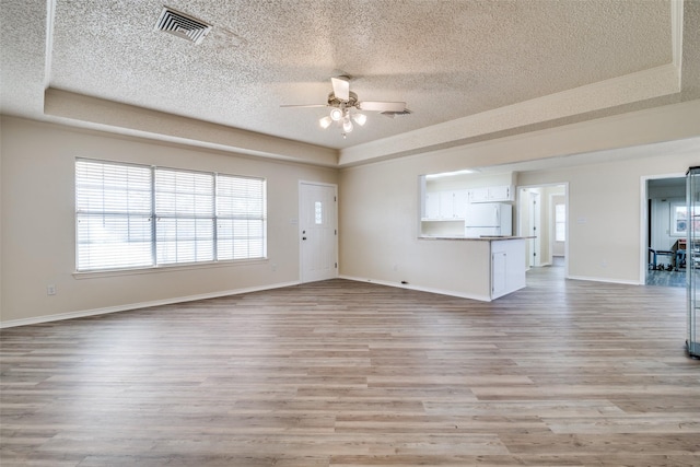 unfurnished living room with ceiling fan, a raised ceiling, light wood-type flooring, and a textured ceiling