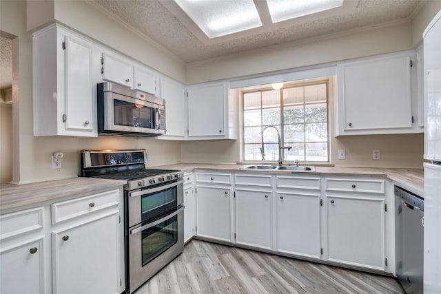 kitchen with white cabinets, sink, a textured ceiling, light hardwood / wood-style floors, and stainless steel appliances