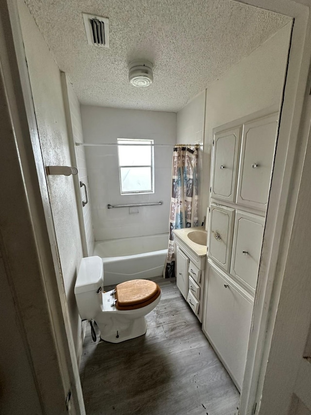 full bathroom featuring toilet, hardwood / wood-style floors, shower / bathtub combination with curtain, a textured ceiling, and vanity