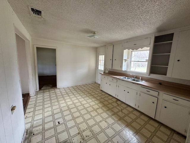 kitchen with a textured ceiling, white cabinets, and sink