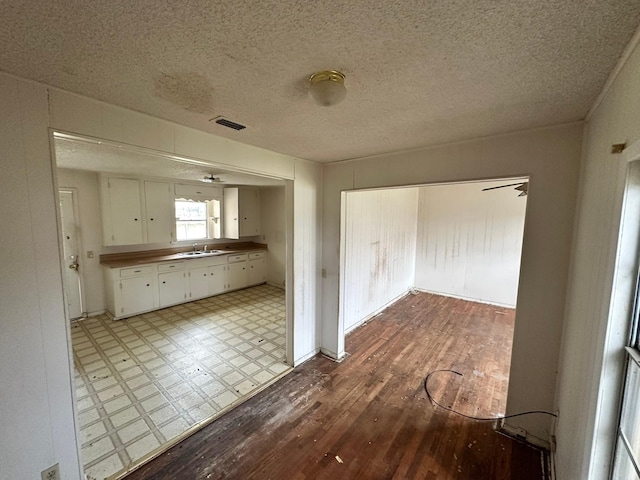 kitchen with ceiling fan, white cabinets, a textured ceiling, light hardwood / wood-style flooring, and sink