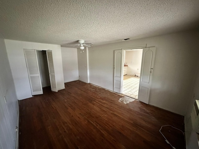 unfurnished bedroom with a textured ceiling, ceiling fan, two closets, and dark hardwood / wood-style floors