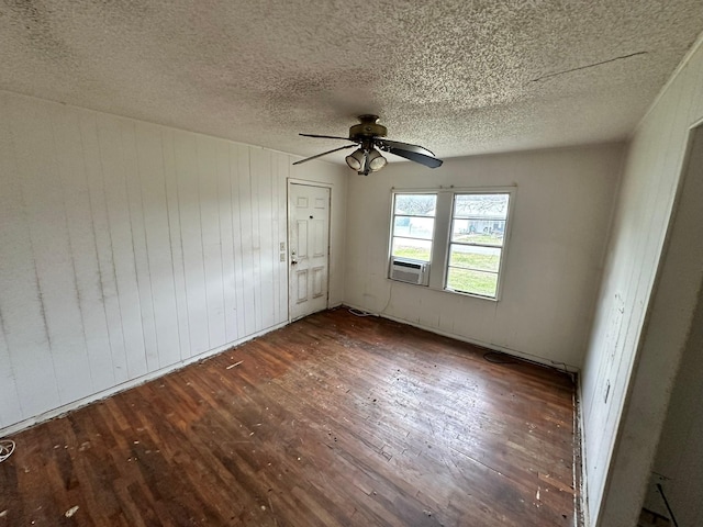 unfurnished room with a textured ceiling, dark wood-type flooring, wood walls, and ceiling fan