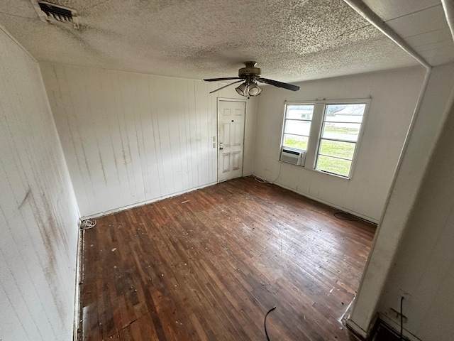 spare room featuring ceiling fan, dark wood-type flooring, cooling unit, and wooden walls