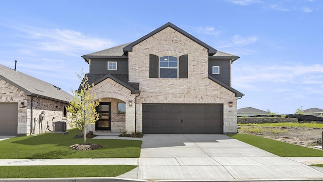 french country home with central air condition unit, driveway, an attached garage, a front lawn, and brick siding
