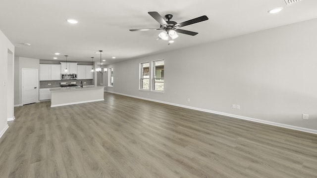 unfurnished living room with baseboards, recessed lighting, and ceiling fan with notable chandelier