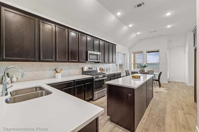 kitchen featuring sink, light wood-type flooring, appliances with stainless steel finishes, a kitchen island, and decorative backsplash